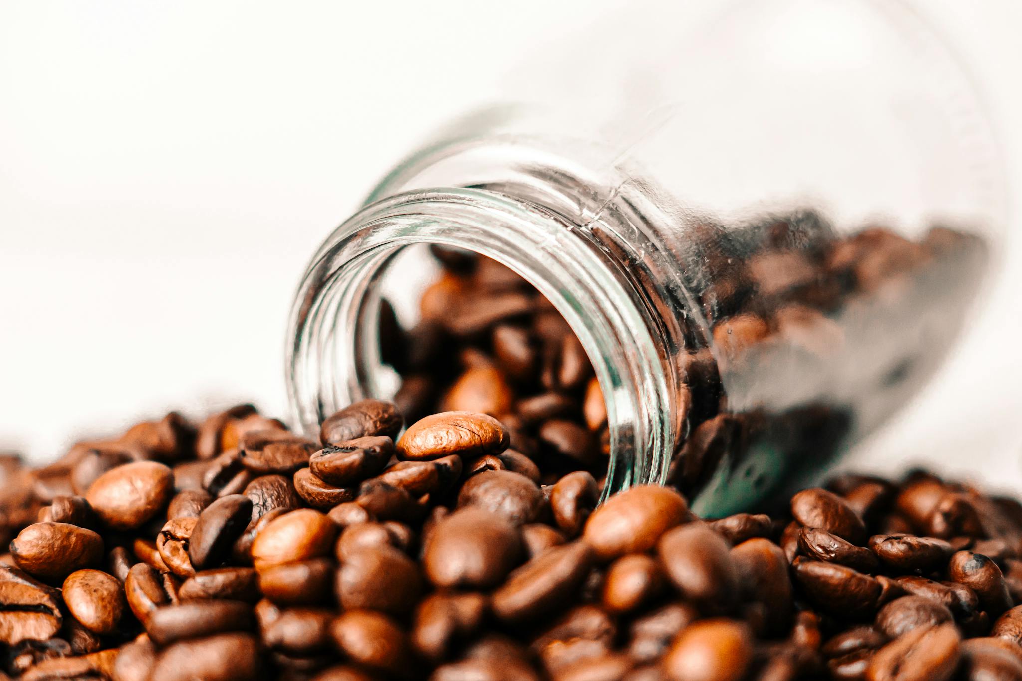 Artistic close-up of roasted coffee beans spilling out of a glass jar, showcasing rich, aromatic textures.