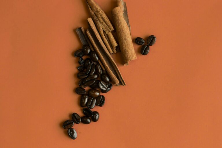 Flat lay of cinnamon sticks and coffee beans on an orange background, perfect for food and spice themes.
